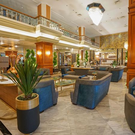Akgun Istanbul Hotel Exterior foto The photo shows a luxurious hotel lobby area. It features stylish seating arrangements with comfortable blue chairs and small coffee tables. The space is well-lit, with elegant chandeliers hanging from the ceiling. There are large potted plants that 