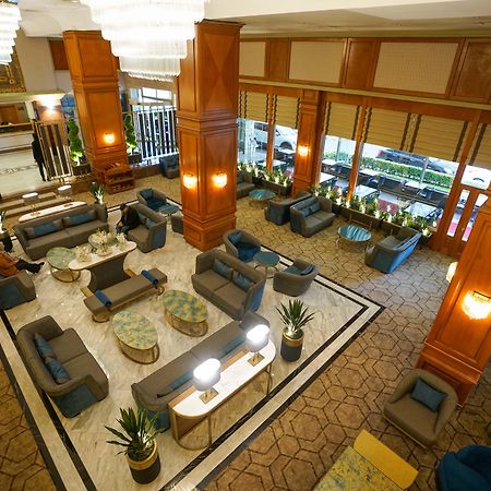 Akgun Istanbul Hotel Exterior foto The photo shows the interior of a hotel lobby. It features a spacious area with elegant wooden pillars and large windows that allow natural light to flow in. There are several seating arrangements with comfortable sofas and chairs, accompanied by rou