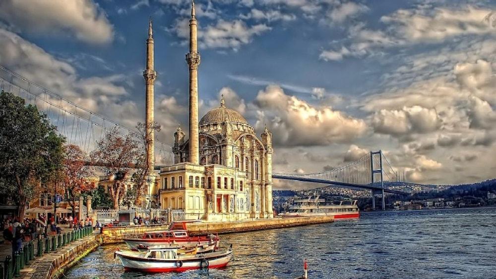 Akgun Istanbul Hotel Exterior foto The photo features a scenic waterfront view that includes a mosque with two tall minarets and a large dome. The architecture appears to be ornate, typical of historic Islamic structures. In the foreground, there are several small boats docked along t