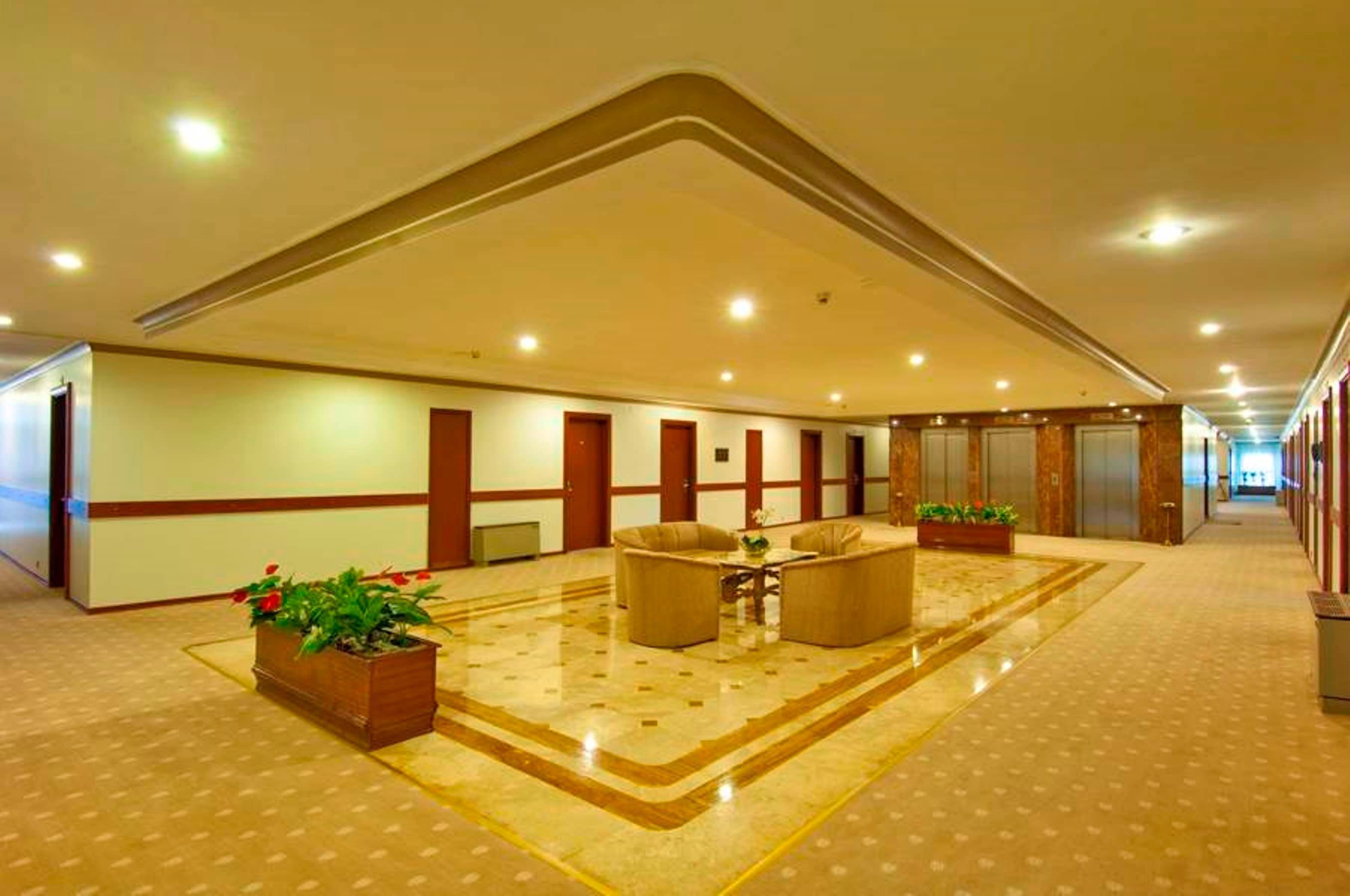 Akgun Istanbul Hotel Exterior foto The photo shows a spacious interior lobby or hallway with a modern design. There are two comfortable chairs positioned around a small table in the center, surrounded by potted plants. The flooring has a patterned design, and the ceiling features a sl
