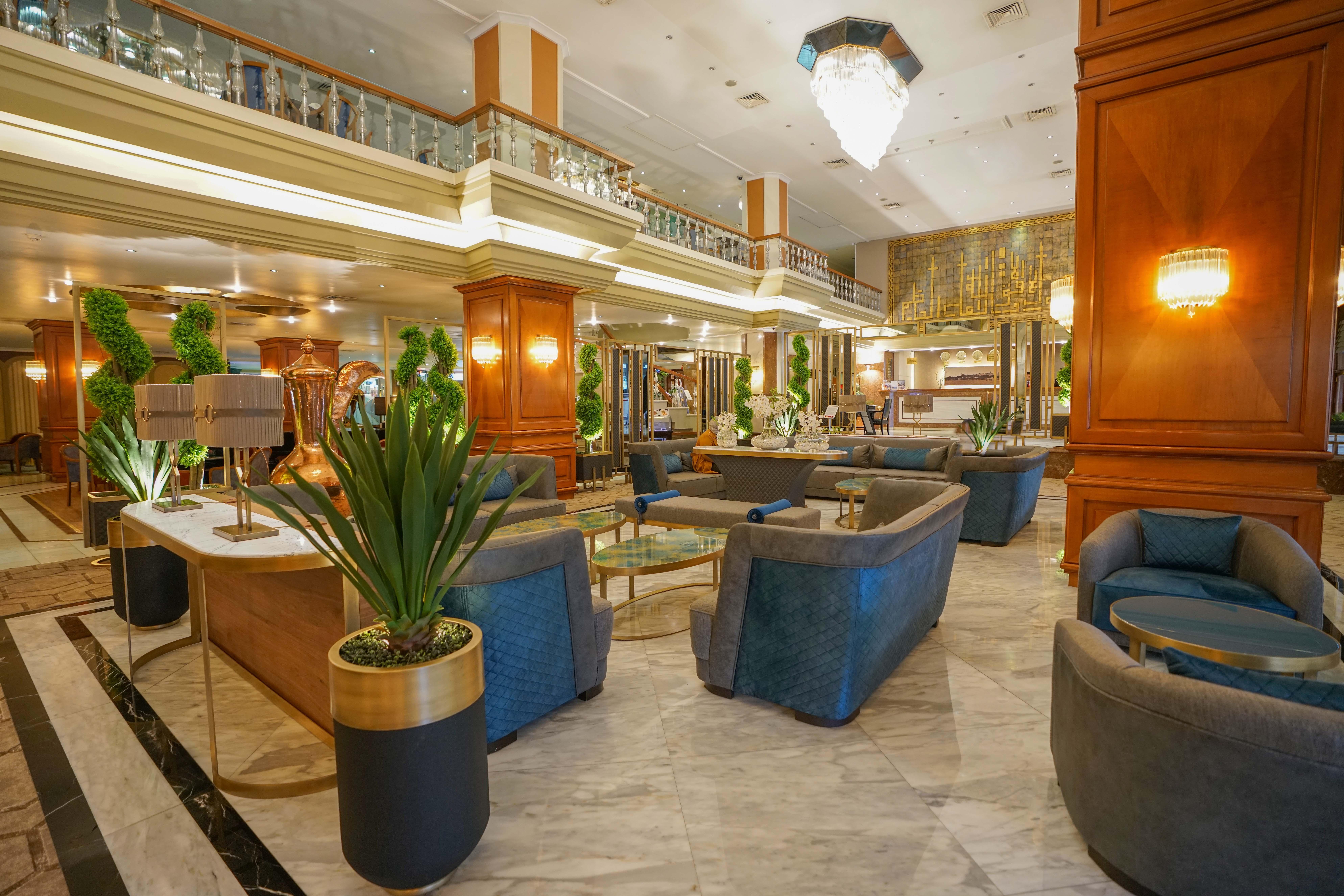 Akgun Istanbul Hotel Exterior foto The photo shows a luxurious hotel lobby area. It features stylish seating arrangements with comfortable blue chairs and small coffee tables. The space is well-lit, with elegant chandeliers hanging from the ceiling. There are large potted plants that 