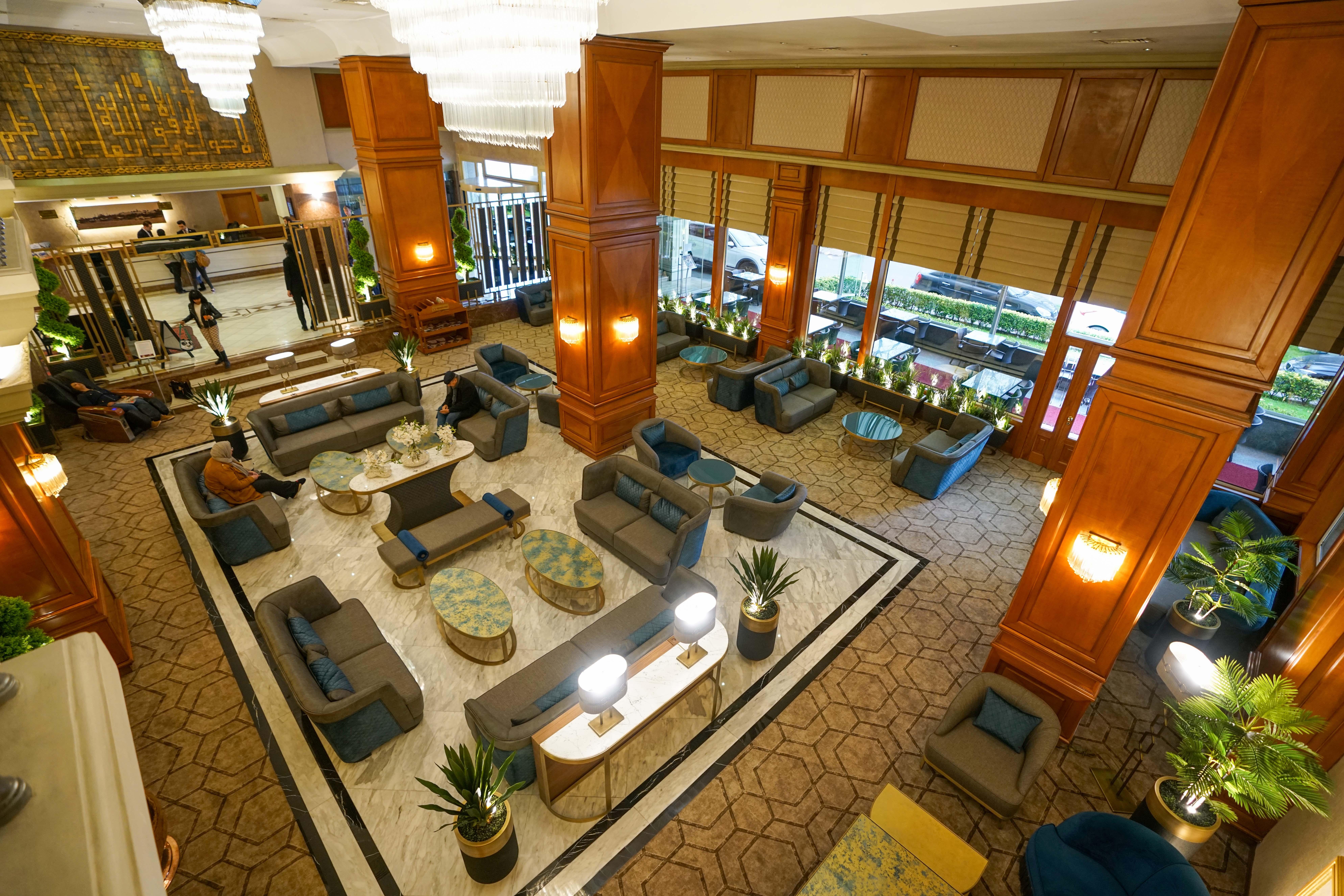 Akgun Istanbul Hotel Exterior foto The photo shows the interior of a hotel lobby. It features a spacious area with elegant wooden pillars and large windows that allow natural light to flow in. There are several seating arrangements with comfortable sofas and chairs, accompanied by rou