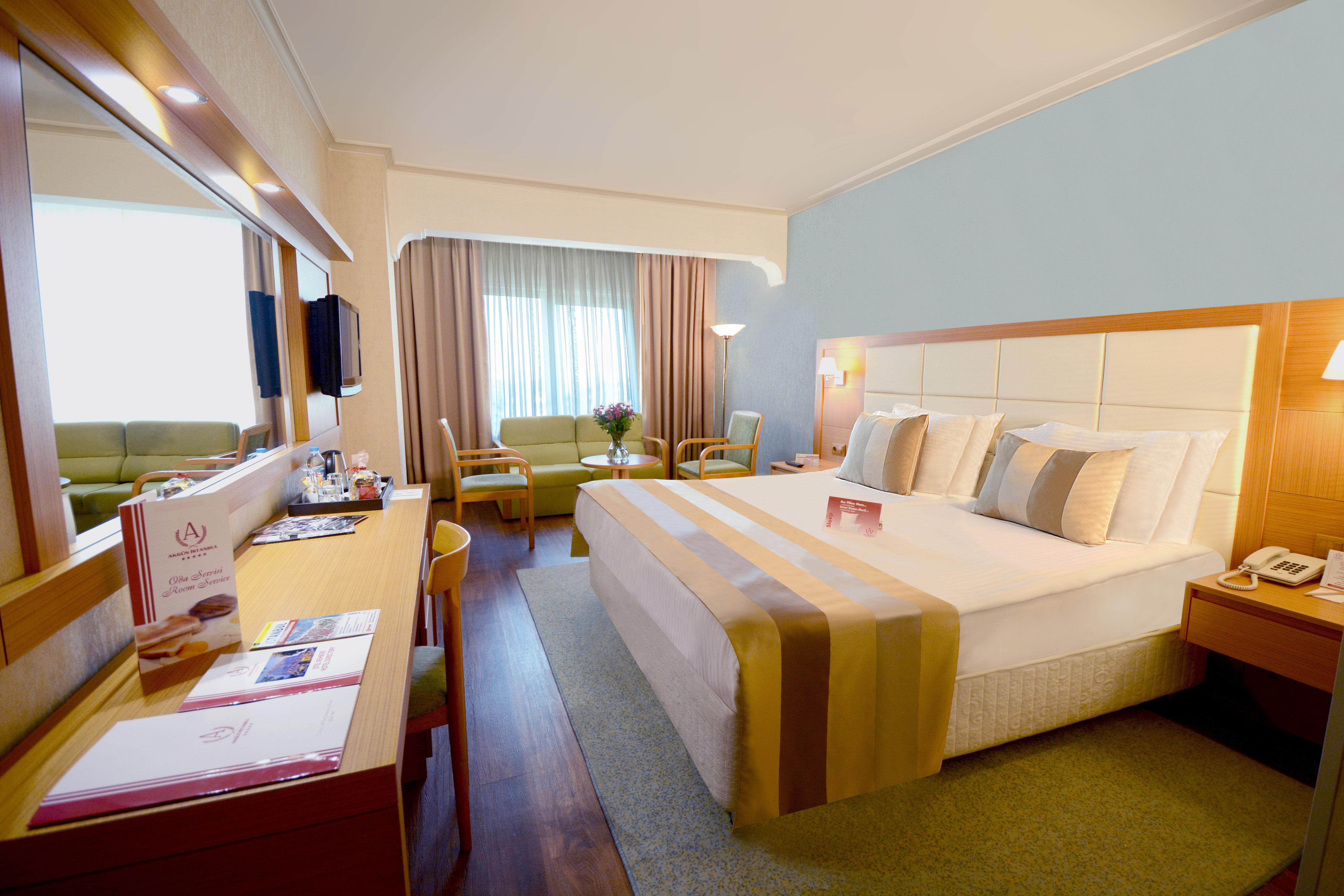 Akgun Istanbul Hotel Exterior foto The photo shows a well-furnished hotel room. It features a large bed with decorative pillows, a desk with a chair, and a seating area that includes a couple of green sofas. There is a large window with light drapes allowing natural light to fill the 