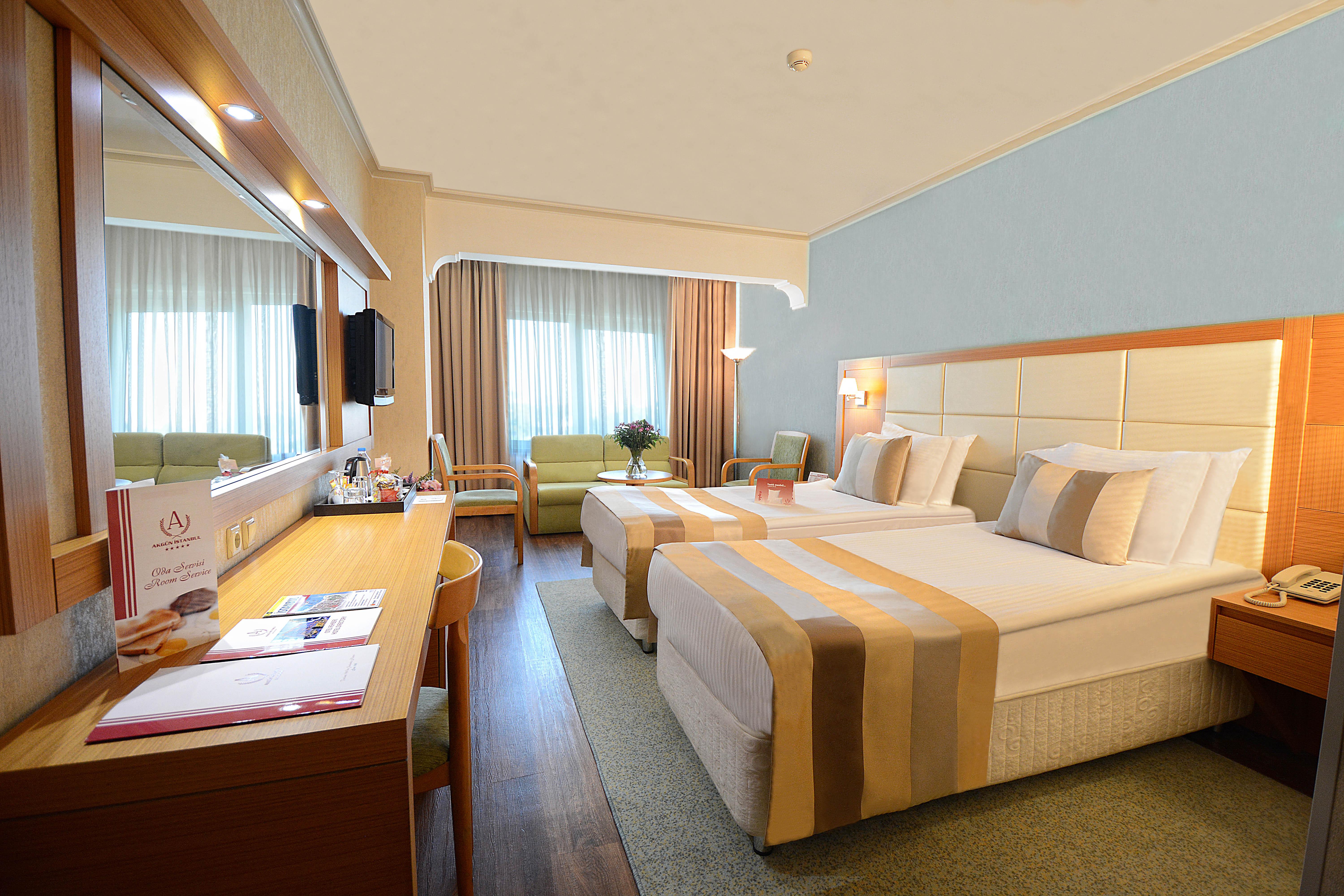 Akgun Istanbul Hotel Exterior foto The photo displays a hotel room featuring two beds with light-colored bedding accented by striped throws. There's a large window allowing natural light to fill the space, along with curtains partially drawn. A wooden desk and chair are positioned nea