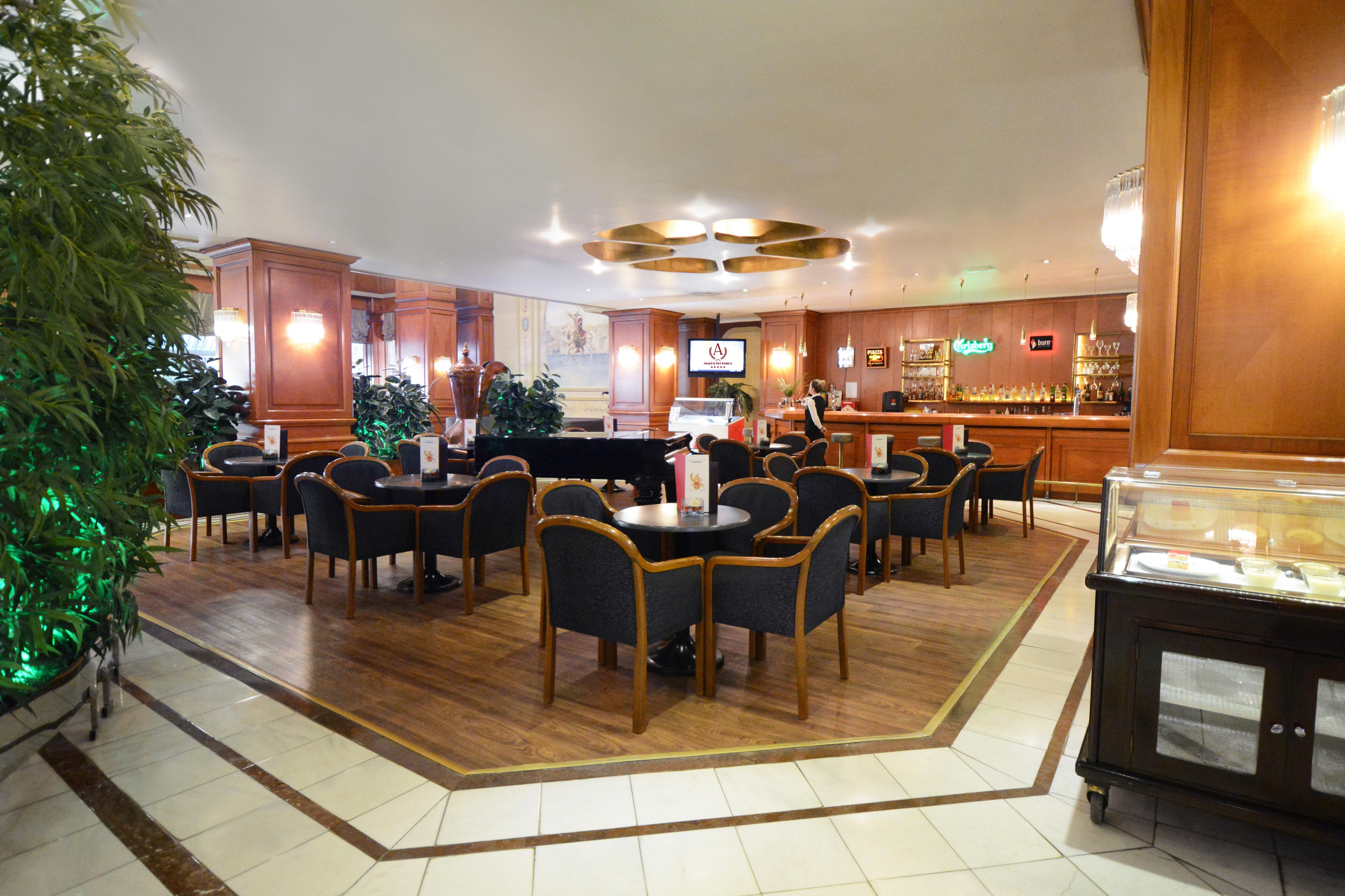 Akgun Istanbul Hotel Exterior foto The photo shows a cozy interior of a lounge or bar area. It features several round tables with dark chairs arranged around them. The space has a warm, inviting atmosphere, characterized by wooden paneling, soft lighting, and decorative plants. In the