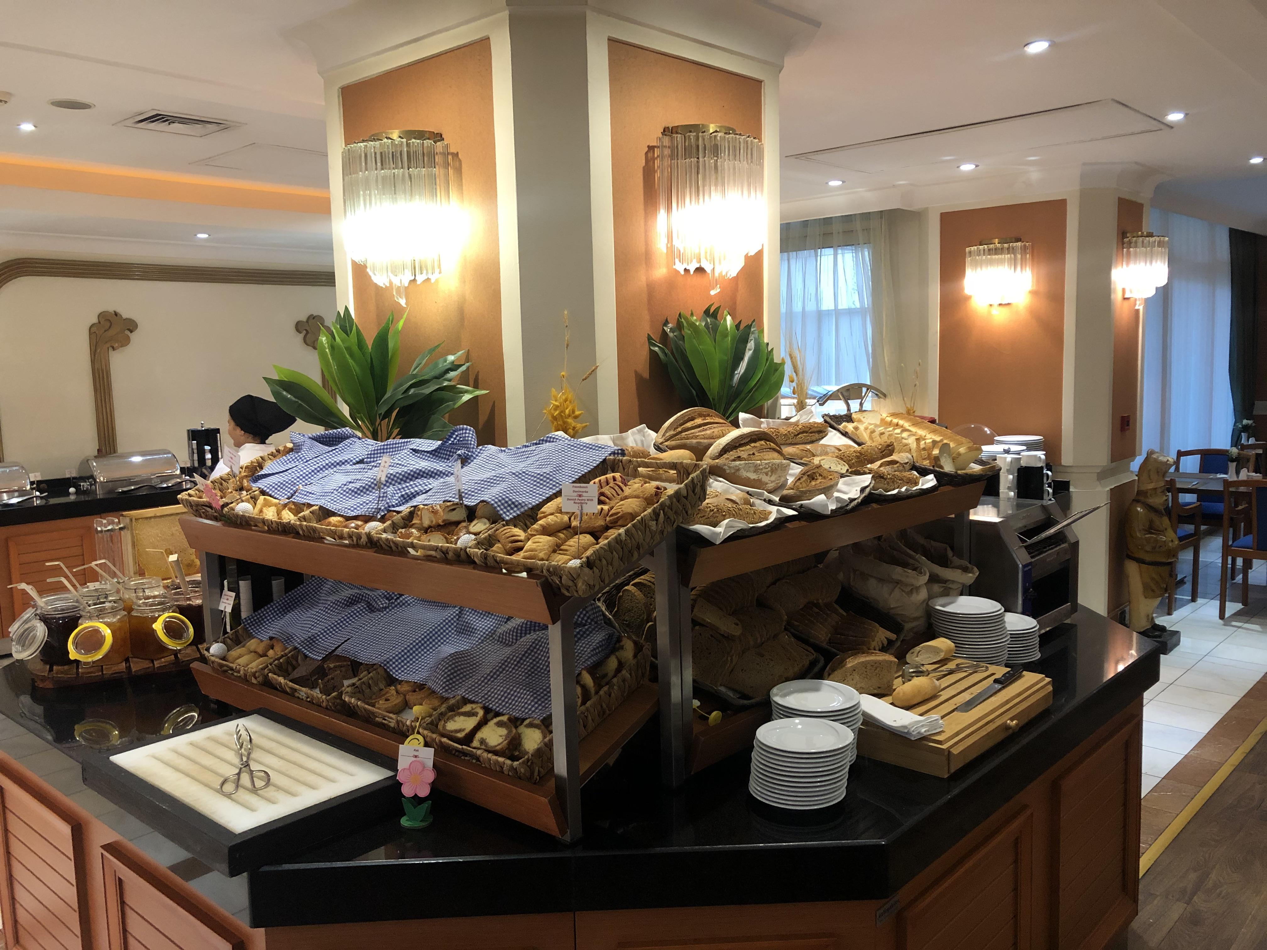 Akgun Istanbul Hotel Exterior foto The photo shows a buffet setup featuring a variety of baked goods. There are two stacked trays filled with different types of bread and pastries, including rolls and loaves, covered with blue napkins. The display is enhanced by decorative plants and 