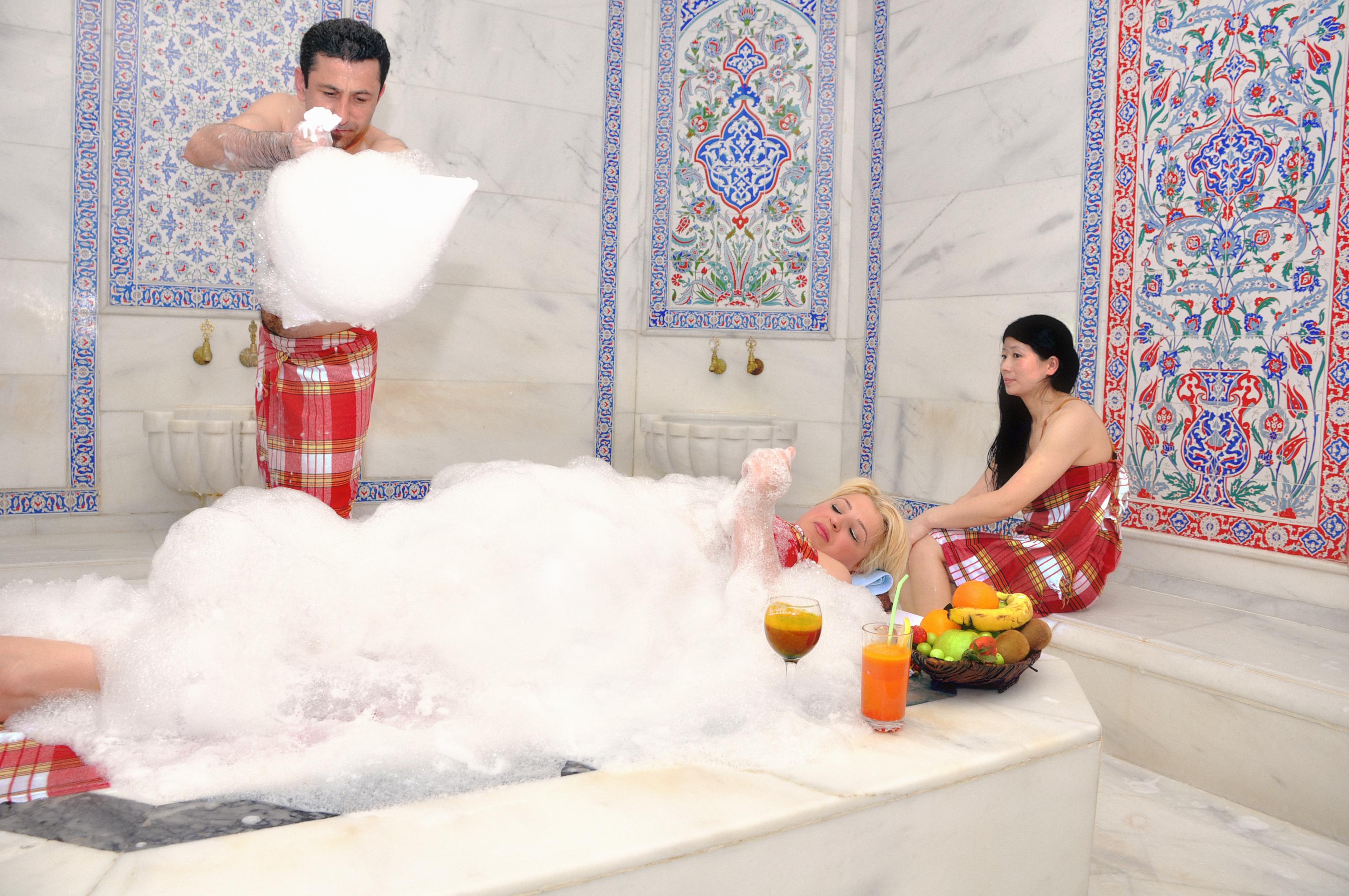 Akgun Istanbul Hotel Exterior foto The image depicts a scene in a luxurious bath setting with ornate tiled walls. There are three individuals present. One person, wearing a checkered towel, is pouring or throwing bubbles, suggesting a playful atmosphere. Another person is lying in a b