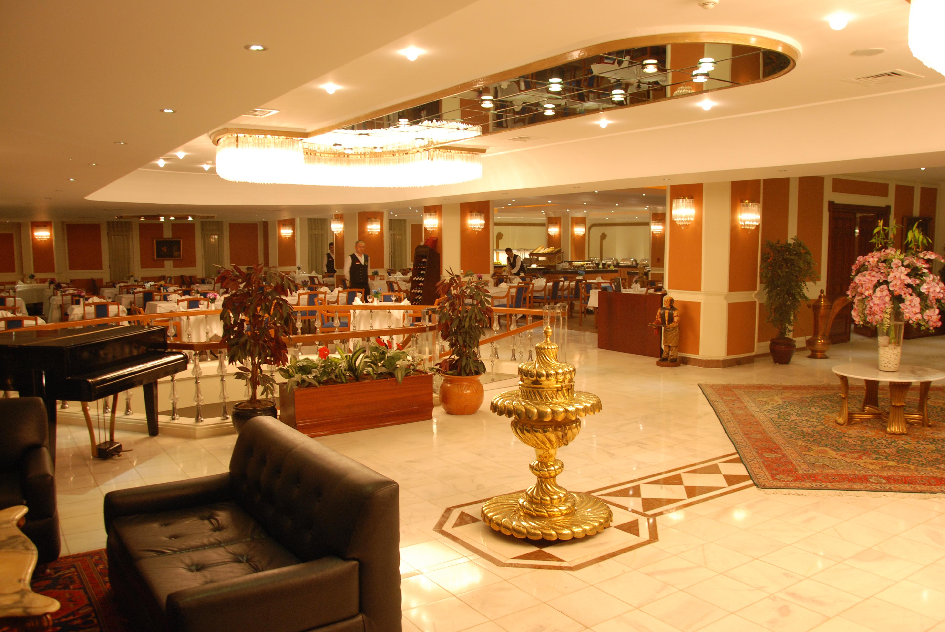 Akgun Istanbul Hotel Exterior foto The photo shows an elegantly designed interior of a restaurant or banquet hall. It features a spacious layout with a beautifully arranged seating area. In the foreground, there is a black couch along with a decorative gold fountain, which adds an opu