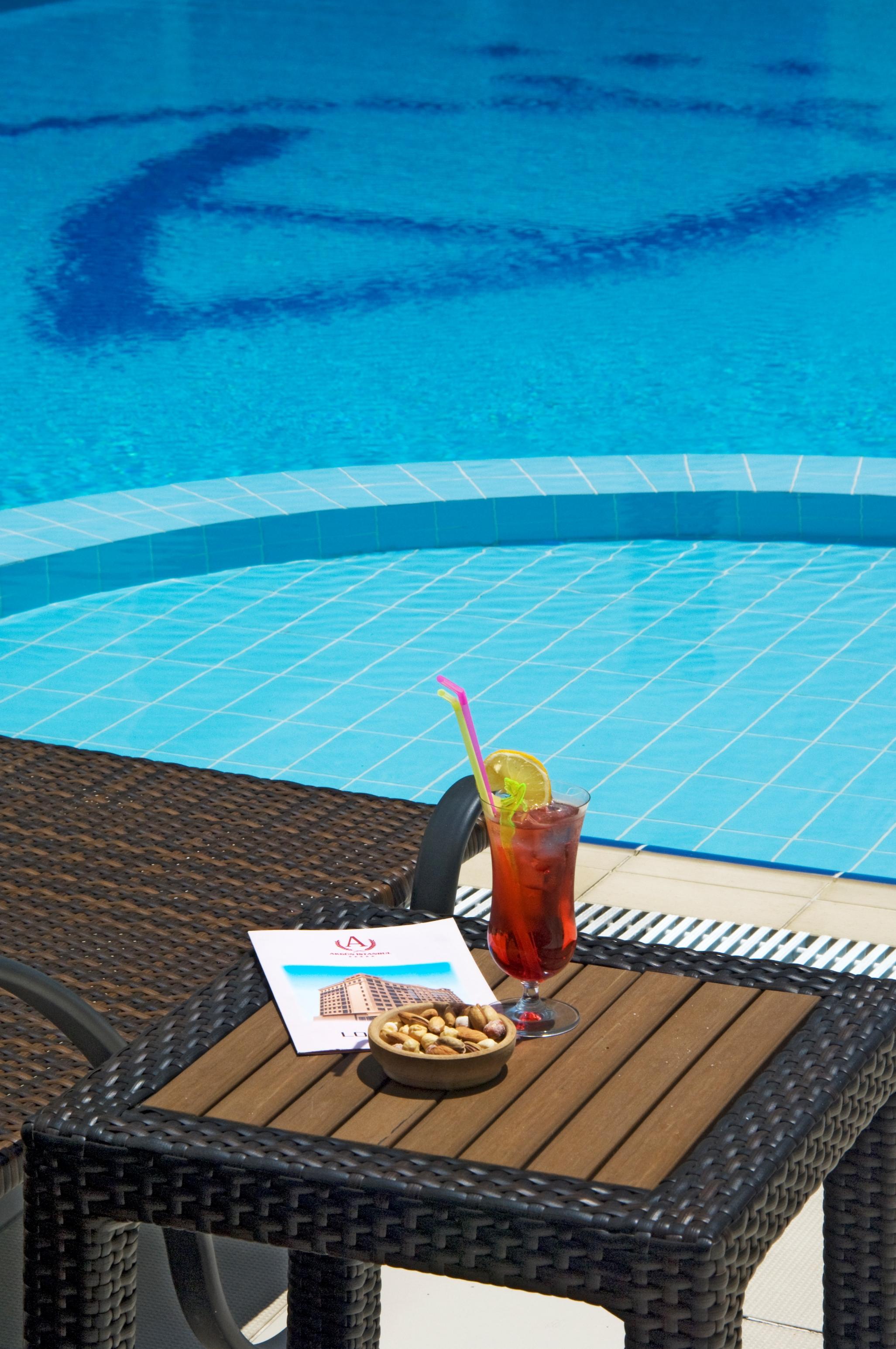 Akgun Istanbul Hotel Exterior foto The photo shows a refreshing cocktail placed on a lounge chair near a swimming pool. The drink is in a tall glass, garnished with a slice of lime and a colorful straw. In the background, there is a bright blue pool with tiles reflecting the sunlight,
