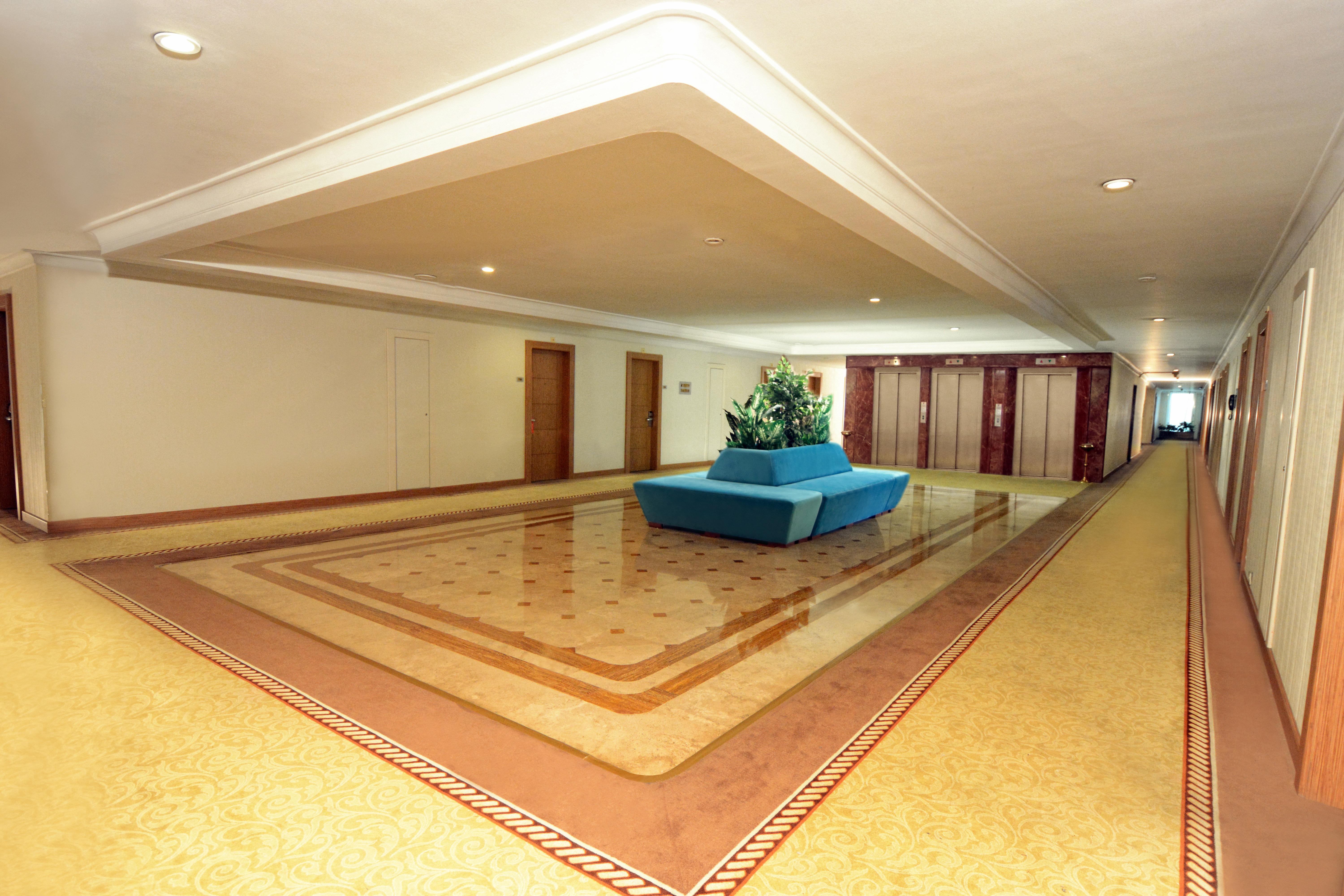 Akgun Istanbul Hotel Exterior foto The photo shows a spacious hallway in a building, likely a hotel or similar establishment. The floor features a decorative design, with a light-colored carpet and a patterned border. In the center of the hallway, there is a blue, modern seating area 