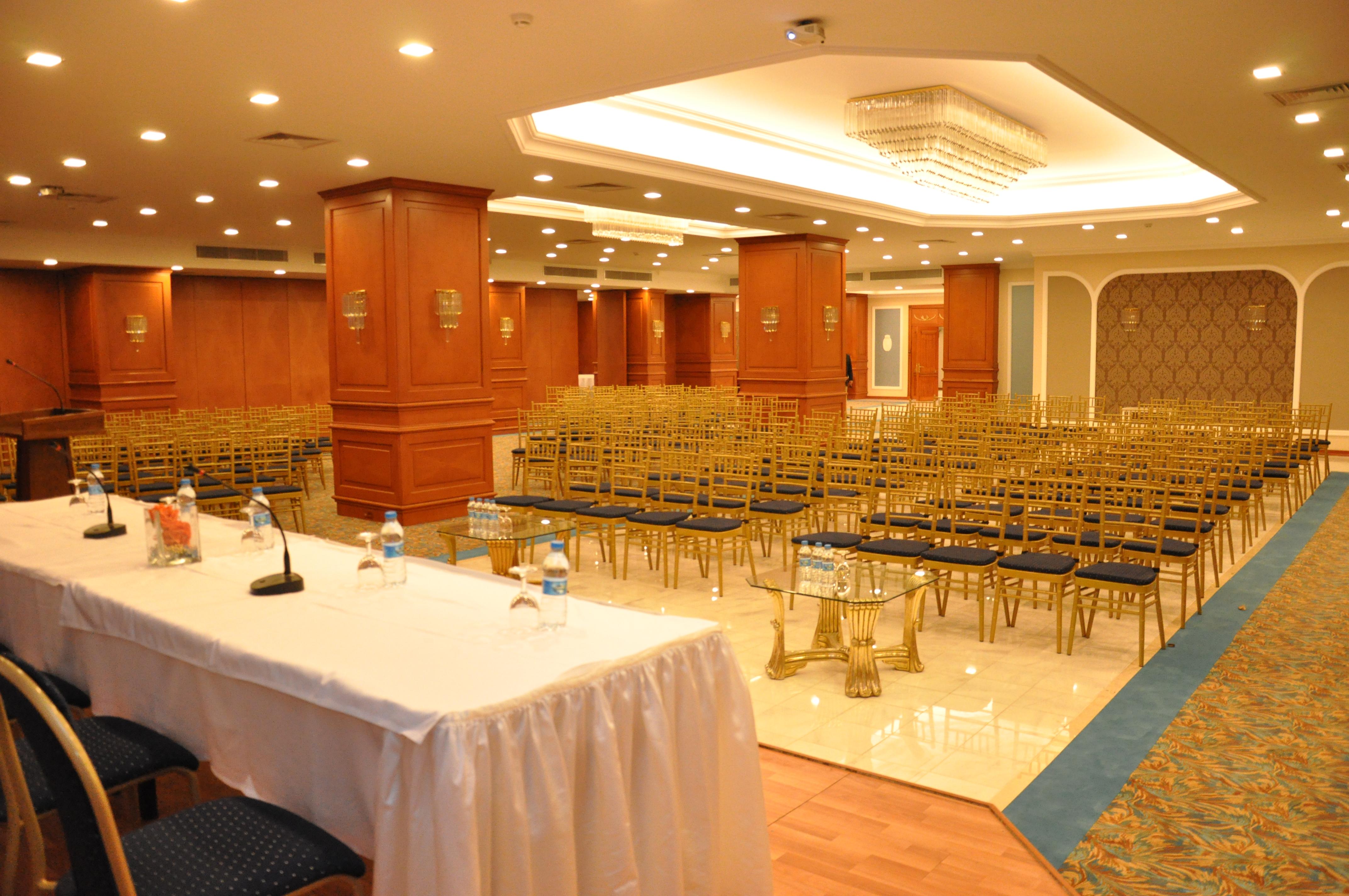 Akgun Istanbul Hotel Exterior foto The photo shows an interior space set up for an event, likely a conference or seminar. There are several rows of empty gold-colored chairs arranged facing a stage or presentation area. In the foreground, there is a table covered with a white cloth, w