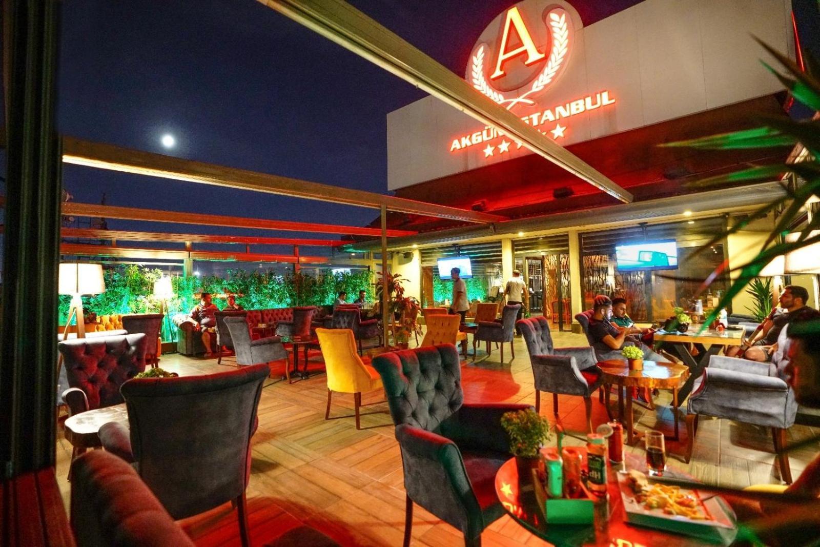 Akgun Istanbul Hotel Exterior foto The photo depicts a vibrant rooftop bar or restaurant setting in the evening. There are several tables and chairs arranged around the space, with guests seated and enjoying their time. The decor features colorful armchairs, and there's a mix of green