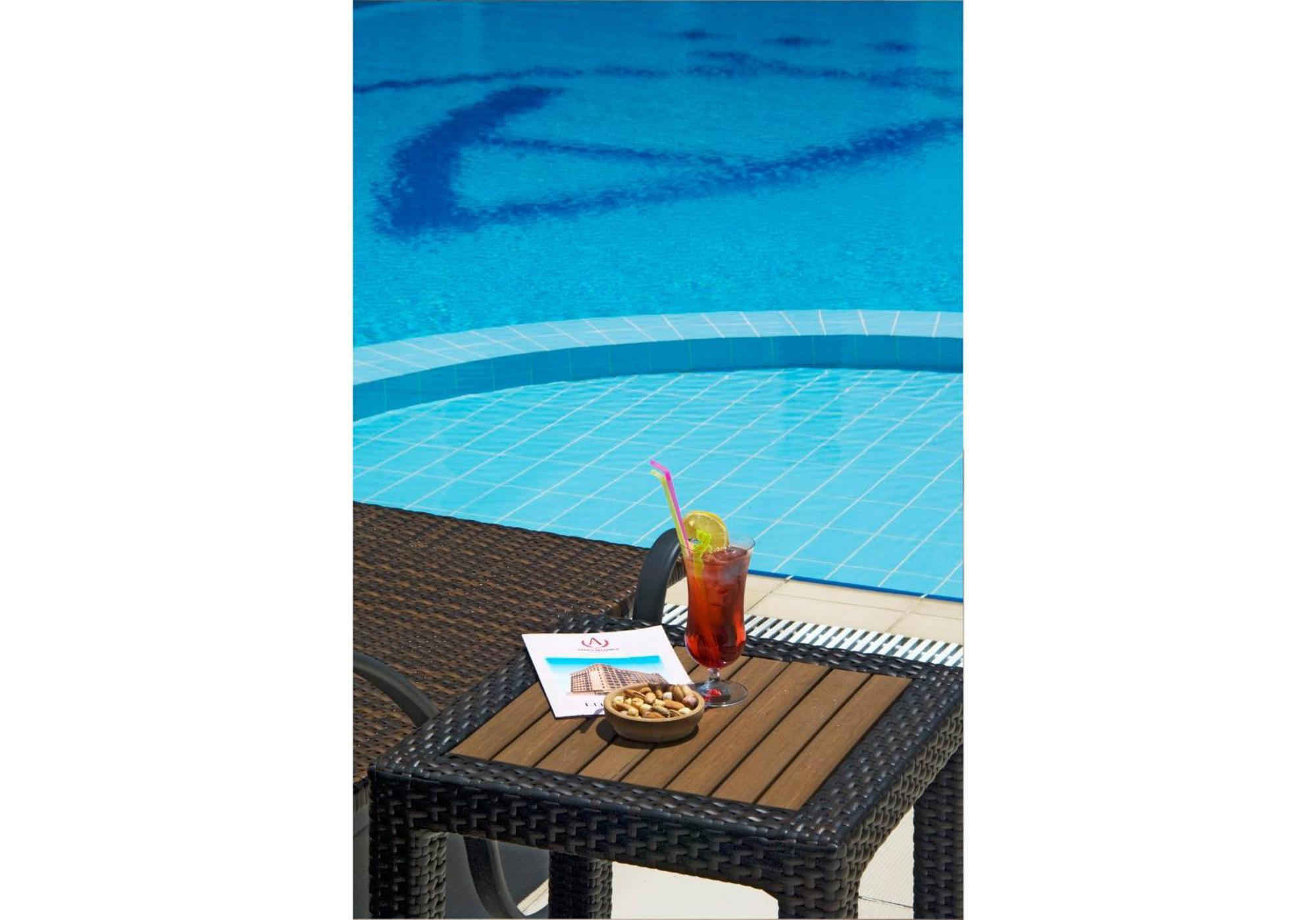 Akgun Istanbul Hotel Exterior foto The photo shows a wicker table beside a swimming pool. On the table, there is a tall glass of a beverage, likely a cocktail, garnished with a slice of lemon, a straw, and ice. There is also a small bowl of snacks, possibly nuts or chips, and a piece 