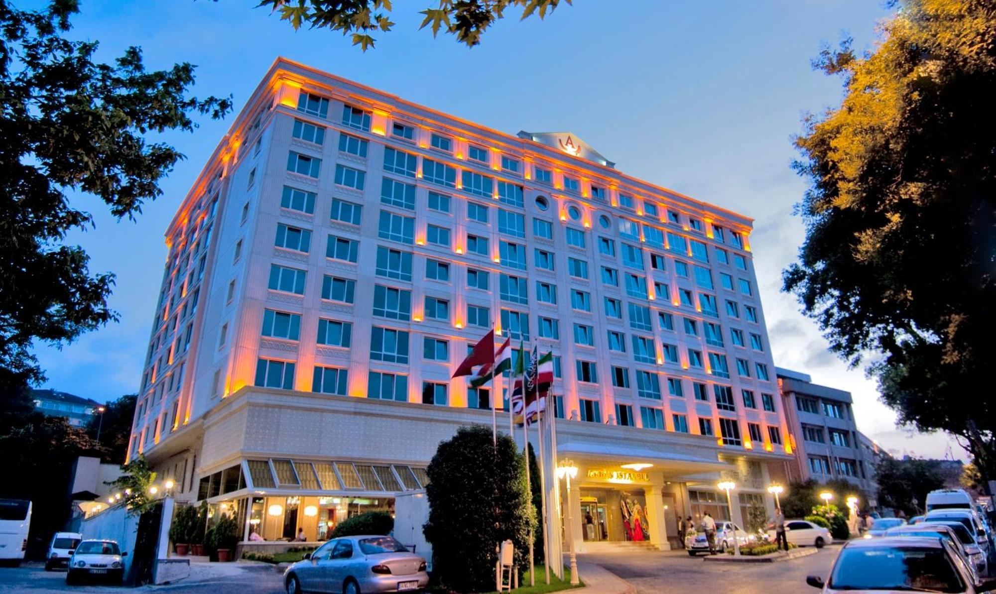 Akgun Istanbul Hotel Exterior foto The photo depicts a tall hotel building with multiple floors, showcased in the evening light. The facade is brightly lit, highlighting its modern architectural design. In front of the hotel, there are several flags, possibly representing different co