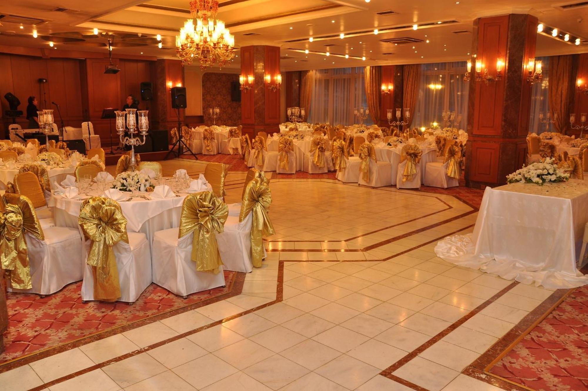 Akgun Istanbul Hotel Exterior foto The photo shows an elegantly decorated banquet hall. The space features several round tables covered with white tablecloths adorned with gold sashes. The chairs are similarly draped in white with gold accents. There are chandeliers hanging from the c