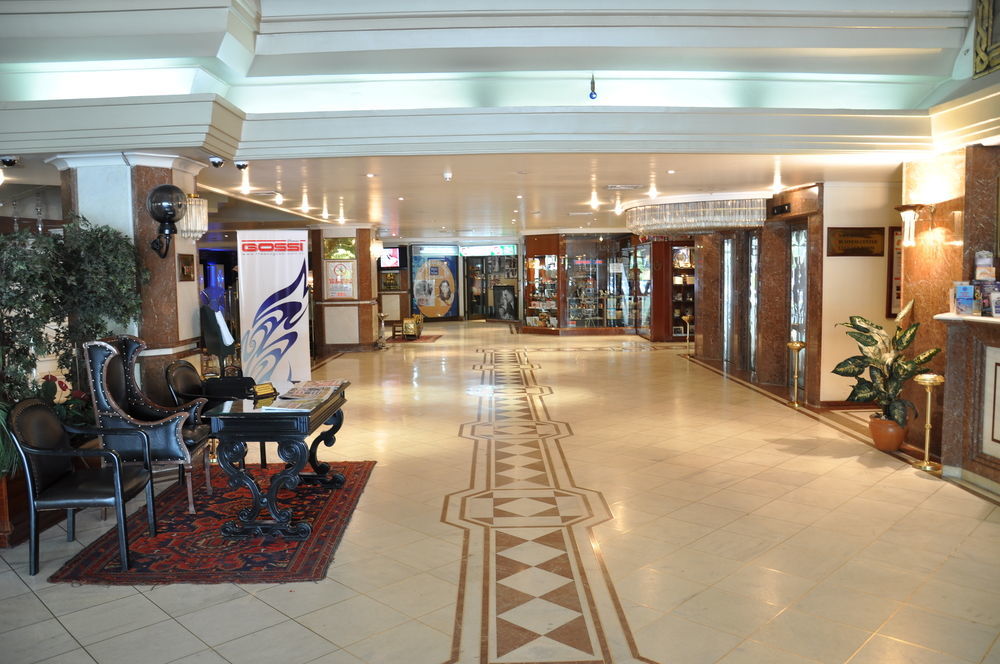 Akgun Istanbul Hotel Exterior foto The photo shows a spacious hallway or lobby area, likely within a hotel or similar establishment. The flooring features decorative tiles with a patterned design. On one side, there are ornate chairs and a small table, adding to the elegant ambiance. 
