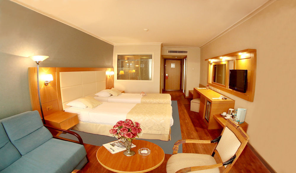Akgun Istanbul Hotel Exterior foto The photo shows a hotel room with a modern and cozy design. There are two single beds with white linens and light beige headboards positioned against the wall. A small seating area features a blue armchair next to a round wooden table, which has a va