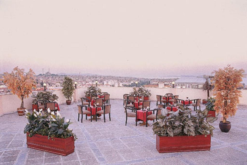 Akgun Istanbul Hotel Exterior foto The photo shows an outdoor dining area set on a rooftop or terrace. It features several tables and chairs arranged for dining, with some tables adorned with red tablecloths. Surrounding the seating area are large planters filled with greenery and dec